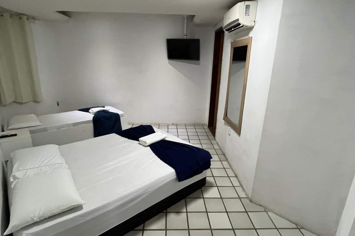 A hotel room with two beds, a TV, an air conditioning unit, and a tiled floor.