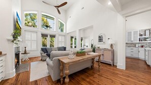 Ein geräumiges Wohnzimmer mit Kamin, einer Couch, einem Holztisch und großen Fenstern mit Blick ins Freie.
