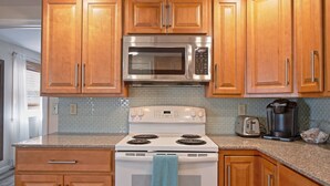 Una cocina con gabinetes de madera, microondas de acero inoxidable, estufa blanca y cafetera.