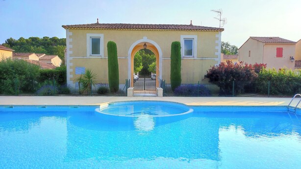 A swimming pool with a clear view of a building with a tiled roof and a gate in the background.