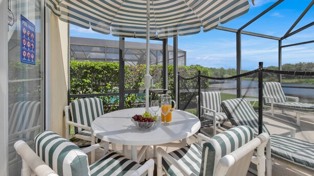A covered outdoor seating area with a table, chairs, and a striped umbrella. - In Orlando area, large Family Friendly Home - Close to Disney (Clermont)