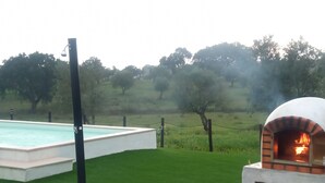 A swimming pool adjacent to a brick outdoor oven, surrounded by a grassy lawn and trees. - Monte Alentejano em Fronteira (Fronteira)