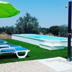 Una piscina con sillones reclinables azules y un paraguas verde.