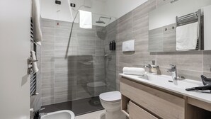 Un baño moderno con ducha envuelta en vidrio, inodoro blanco y tocador de madera con lavabo y espejo.