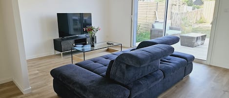 A modern living room with a large dark blue sofa, a glass coffee table, and a flat-screen TV on a black stand.