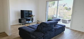 A modern living room with a large flat-screen TV, a dark blue sofa, and a glass coffee table. - Les Maisons de la Plage (Saint-Philibert)