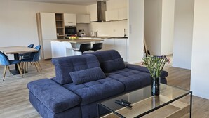 Ein modernes Wohnzimmer mit einem blauen Sofa, einem Glastisch und einem Essbereich mit einem Holztisch und blauen Stühlen.