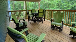 A covered deck with wooden flooring, green Adirondack chairs, a table, and chairs. - Quiet cabin 30 min from wineries, restaurants, Sugar Creek & Walnut Creek.  (Fresno)