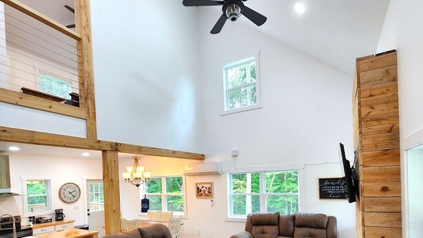 A spacious living area with a high ceiling, wooden beams, and a ceiling fan. There are three brown leather sofas and a wooden accent wall. - Quiet cabin 30 min from wineries, restaurants, Sugar Creek & Walnut Creek.  (Fresno)