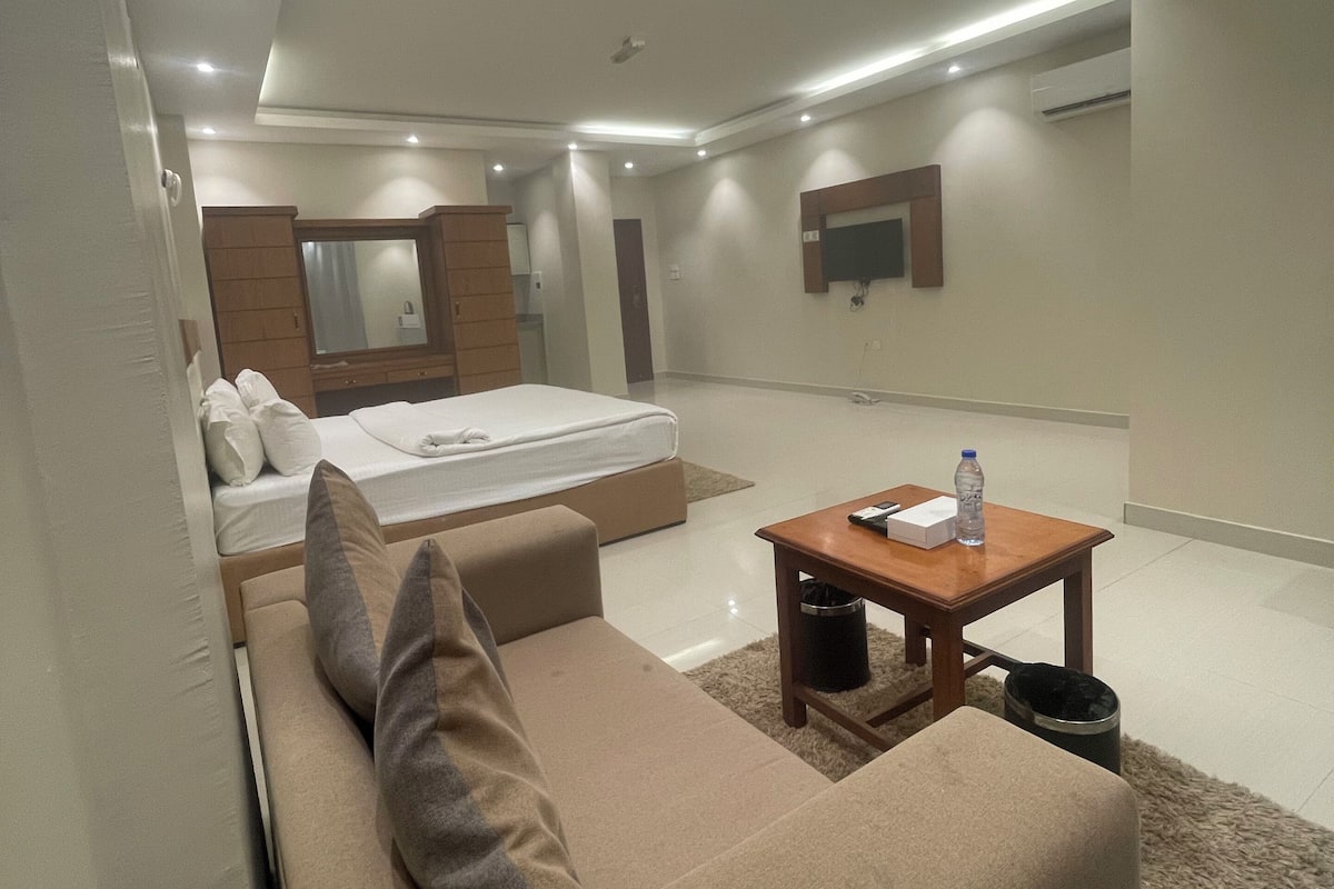 A modern bedroom with a bed, a sofa, a small table, and a mirror.