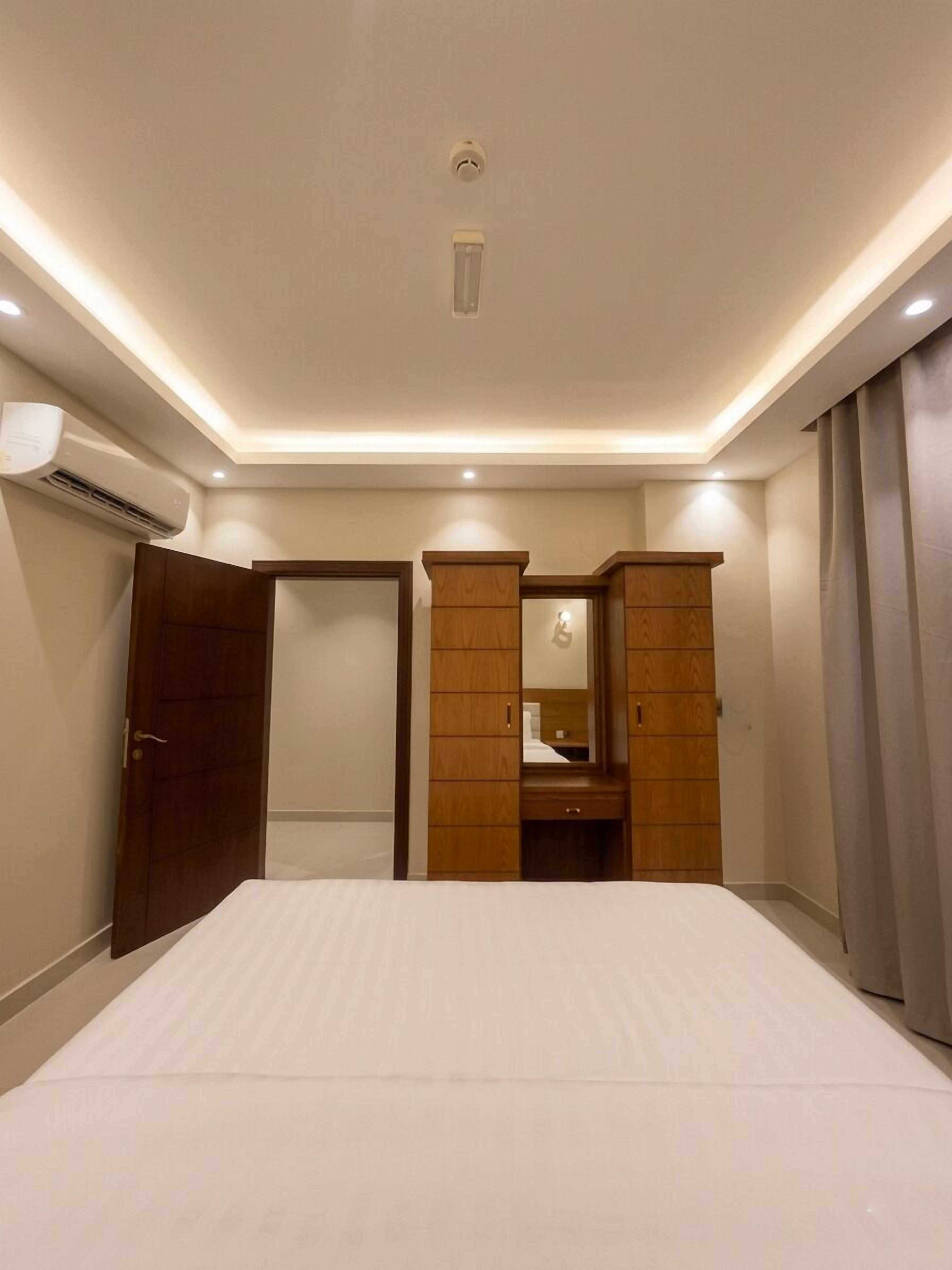 A bedroom with a bed, a wooden wardrobe, a mirror, and an air conditioning unit.