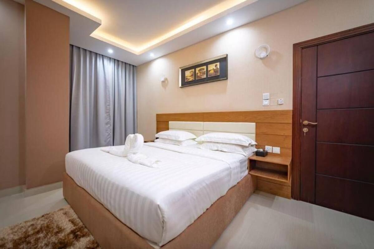A hotel room with a large bed, a wooden headboard, a bedside table, a wardrobe, and a ceiling light fixture.
