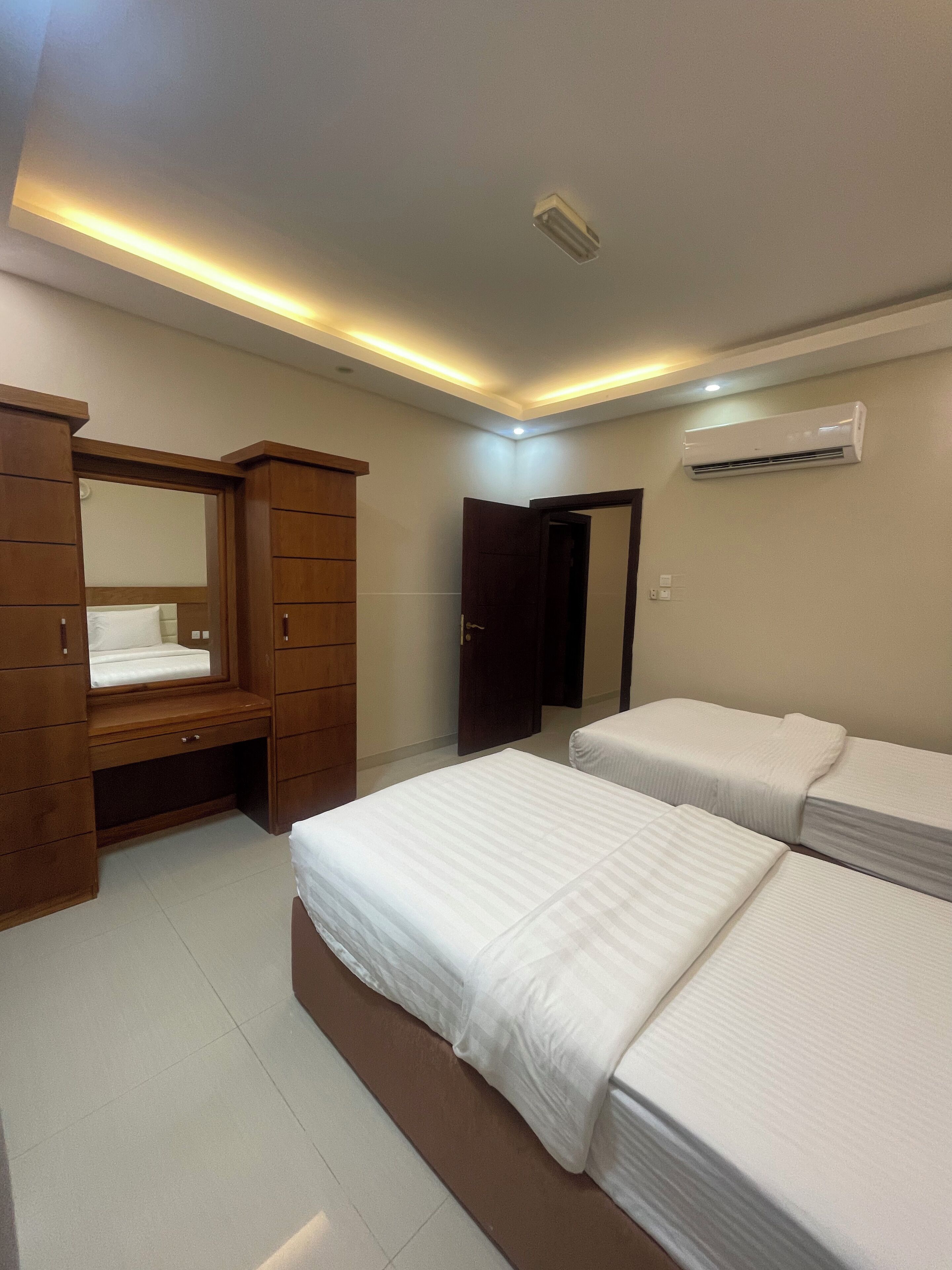 Une chambre avec deux lits, une armoire en bois, un miroir et un appareil de climatisation.