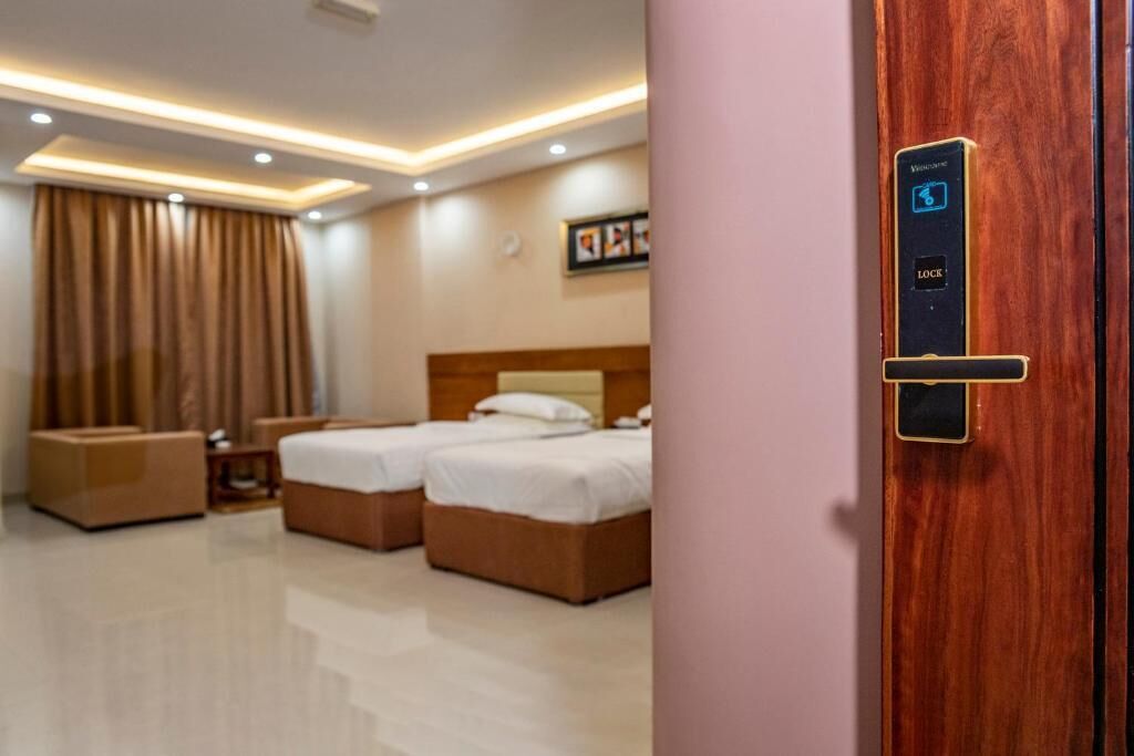 Habitación de hotel con puerta de madera, cama, mesita de noche, silla y un cuadro colgado en la pared.