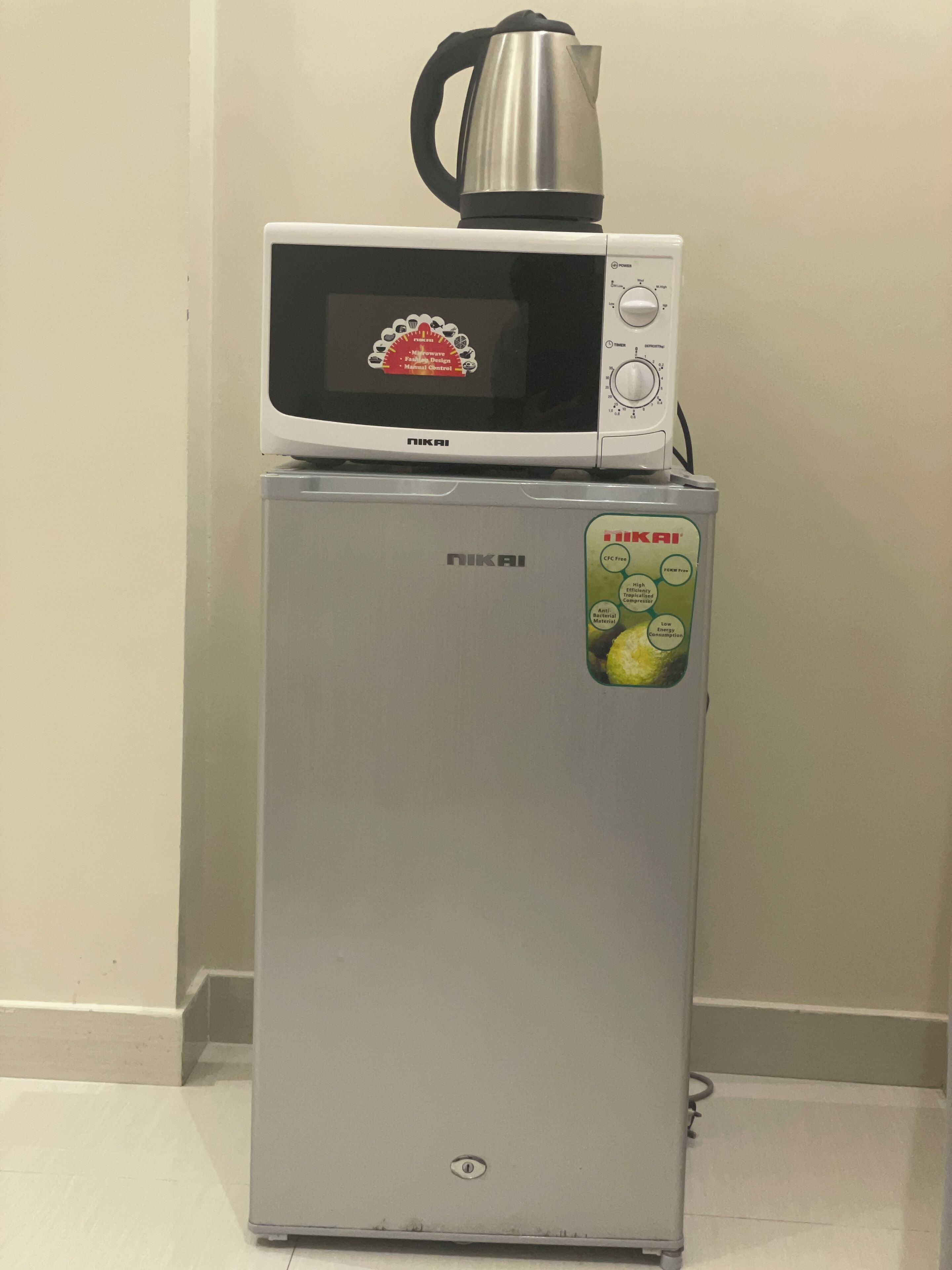Ein Kühlschrank mit einer Mikrowelle darauf, einem Aufkleber an der Seite und einem Wasserkocher auf der Mikrowelle.