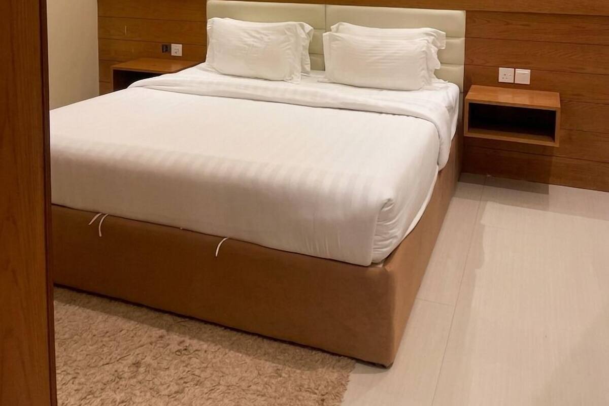 A neatly arranged bedroom with a large bed, bedside tables, and wall-mounted lighting.
