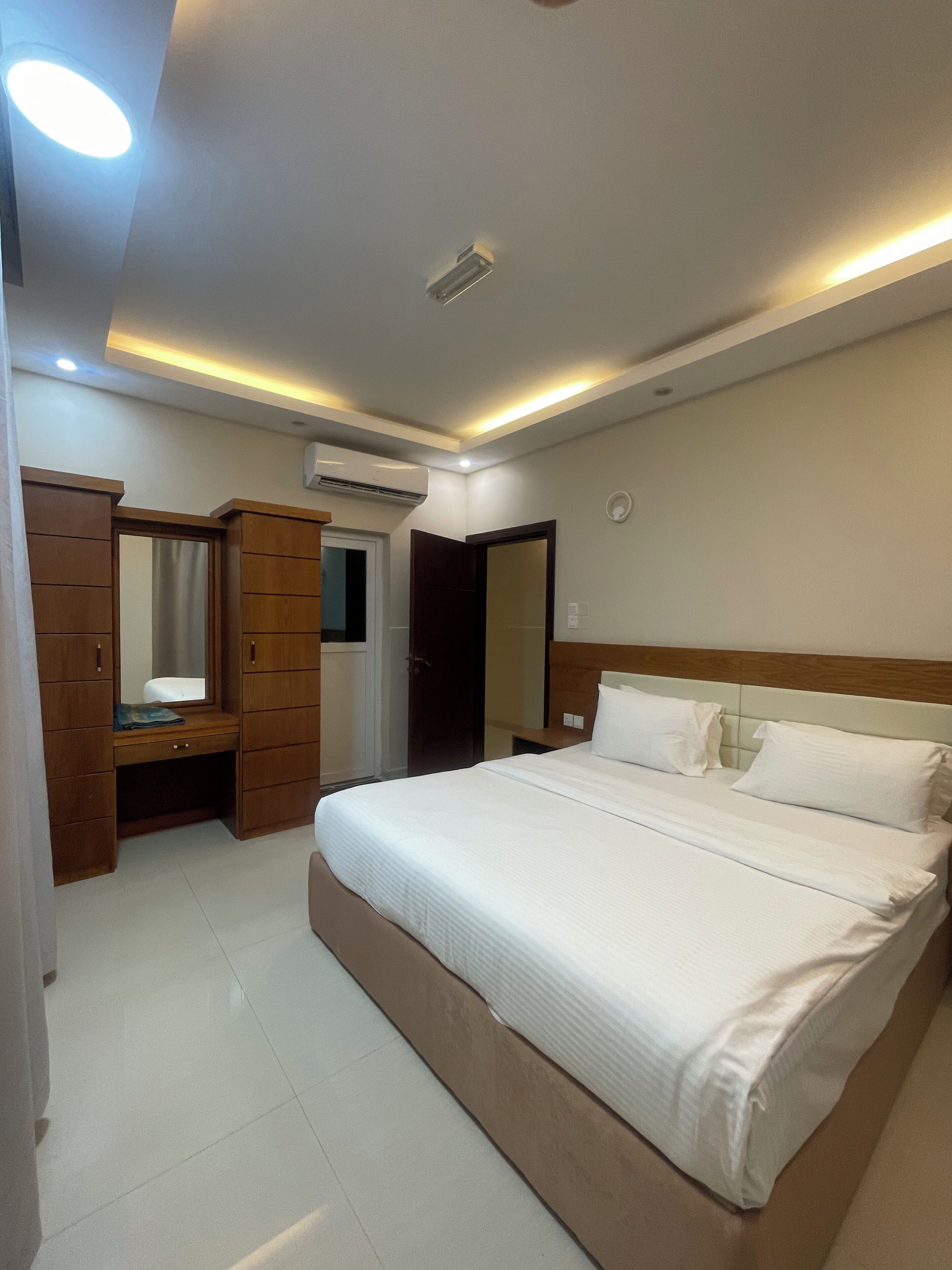 A bedroom with a bed, a wooden wardrobe, a mirror, and an air conditioning unit.
