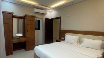A bedroom with a bed, a wooden wardrobe, a mirror, and an air conditioning unit.