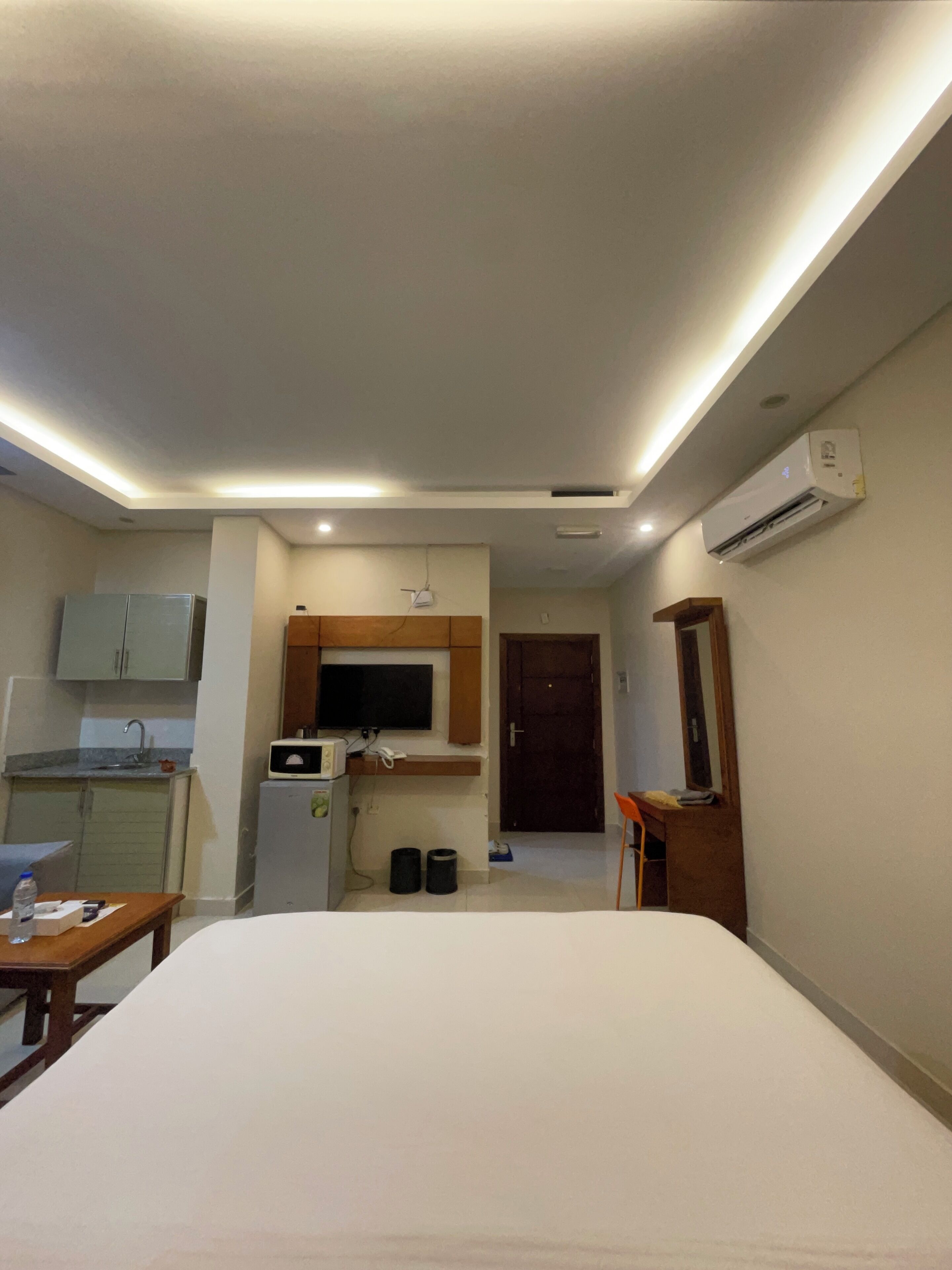 A hotel room with a bed, a small kitchenette, a television, and an air conditioning unit.