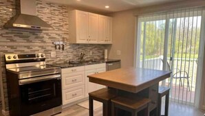 A modern kitchen with a stainless steel oven, white cabinets, a hutch, and a large island with stools. - Country Retreat One (North Tonawanda)
