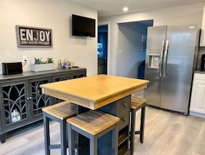 Eine Küche mit Holztisch und Barhocker, einem Edelstahl-Kühlschrank und einem an der Wand montierten Fernseher.