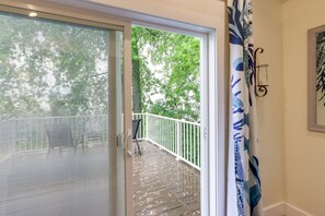 Una terraza de madera con barandal blanco, un cristal que da a un balcón y una cortina azul y blanca estampada.