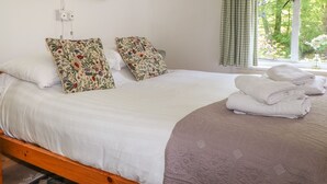 Un letto ben rifatto con cuscini a fiori, un piumone bianco e asciugamani arrotolati su una struttura in legno.