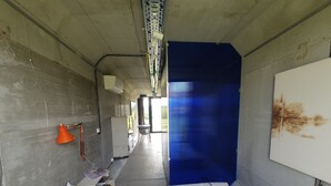 Un pasillo estrecho con una cama, una puerta azul y una pared blanca con un cartel.