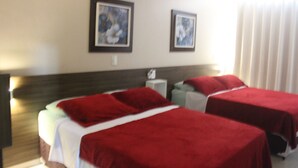 Ein Hotelzimmer mit zwei Betten, beide mit roter Bettwäsche bezogen. Darüber hängen zwei gerahmte Bilder an der Wand.