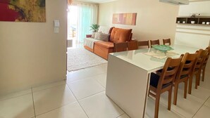 Ein modernes Wohnzimmer mit Sofa, Esstisch mit Stühlen und einer Küchenzeile mit Schränken und einer Pendelleuchte.