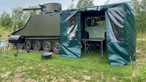 A military vehicle with a tent-like structure attached, featuring a table and chairs inside. - Glamping Samaritan tank (Boston)