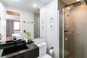 A modern bathroom with a black countertop, a toilet, a glass shower enclosure, and framed pictures on the wall.