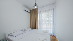 Ein sauberes, modernes Hotelzimmer mit zwei Betten, einem Nachttisch, einer Klimaanlage und Blick ins Freie durch transparente Vorhänge.