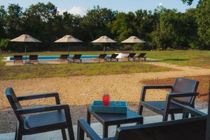 A poolside area with lounge chairs and umbrellas, a table with a tray and a bottle, and a view of the pool and trees. - KOKO village-1 (Gornji Kokoti)