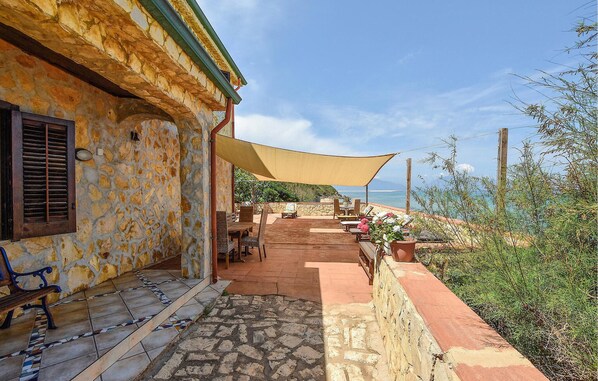 Un bâtiment en pierre doté d’un patio aménagé avec du mobilier d’extérieur et d’un grand auvent.