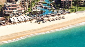 An aerial view of a beachfront hotel with multiple swimming pools, beach umbrellas, and a sandy beach. - BISBEE WEEK (Cabo San Lucas)