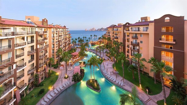 A hotel with multiple floors, a central swimming pool, and a view of the sea. - BISBEE WEEK (Cabo San Lucas)