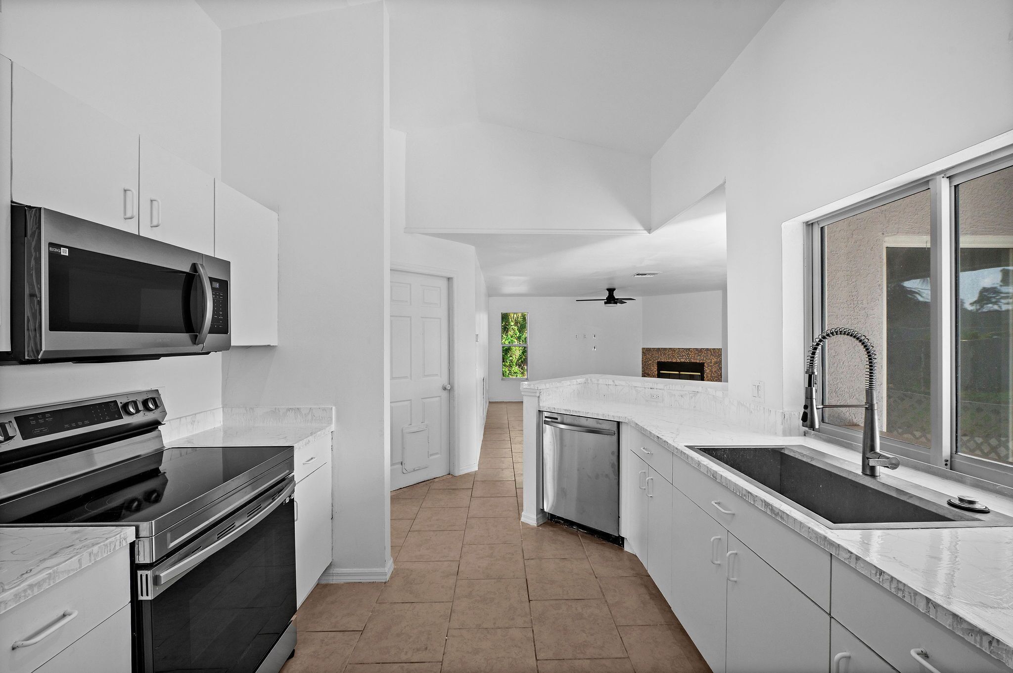 A modern kitchen with stainless steel appliances, white cabinetry, and a large window providing natural light.