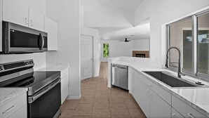 A modern kitchen with stainless steel appliances, white cabinetry, and a large window providing natural light. - Newly Updated House on Double Lot (North Port)