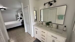 A bedroom with a bed, a bathroom with a sink, mirror, and cabinets. - Newly Updated House on Double Lot (North Port)