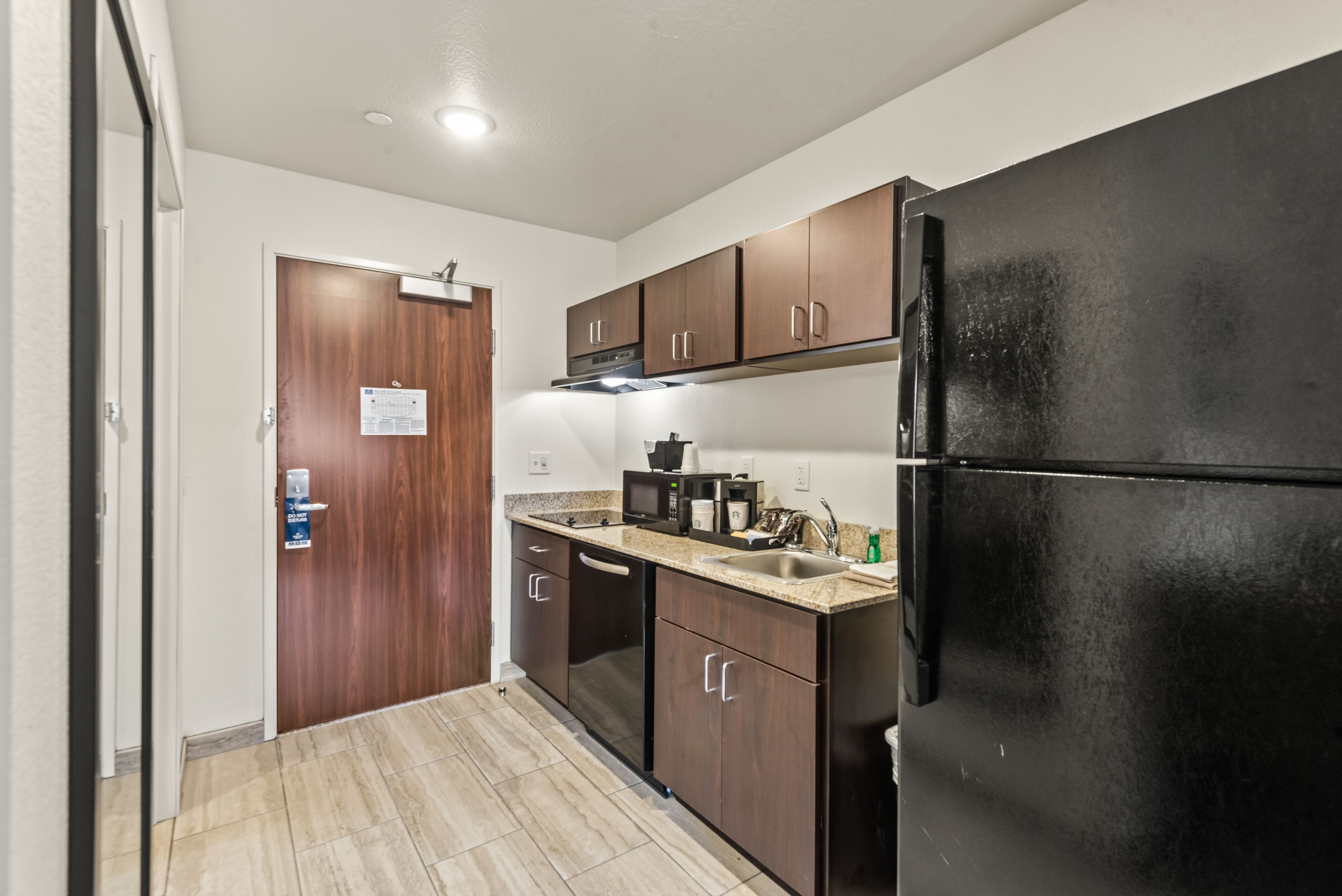 A compact kitchen with dark wooden cabinets, a black refrigerator, and a stainless steel sink.