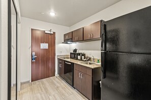 A compact kitchen with dark wooden cabinets, a black refrigerator, and a stainless steel sink.