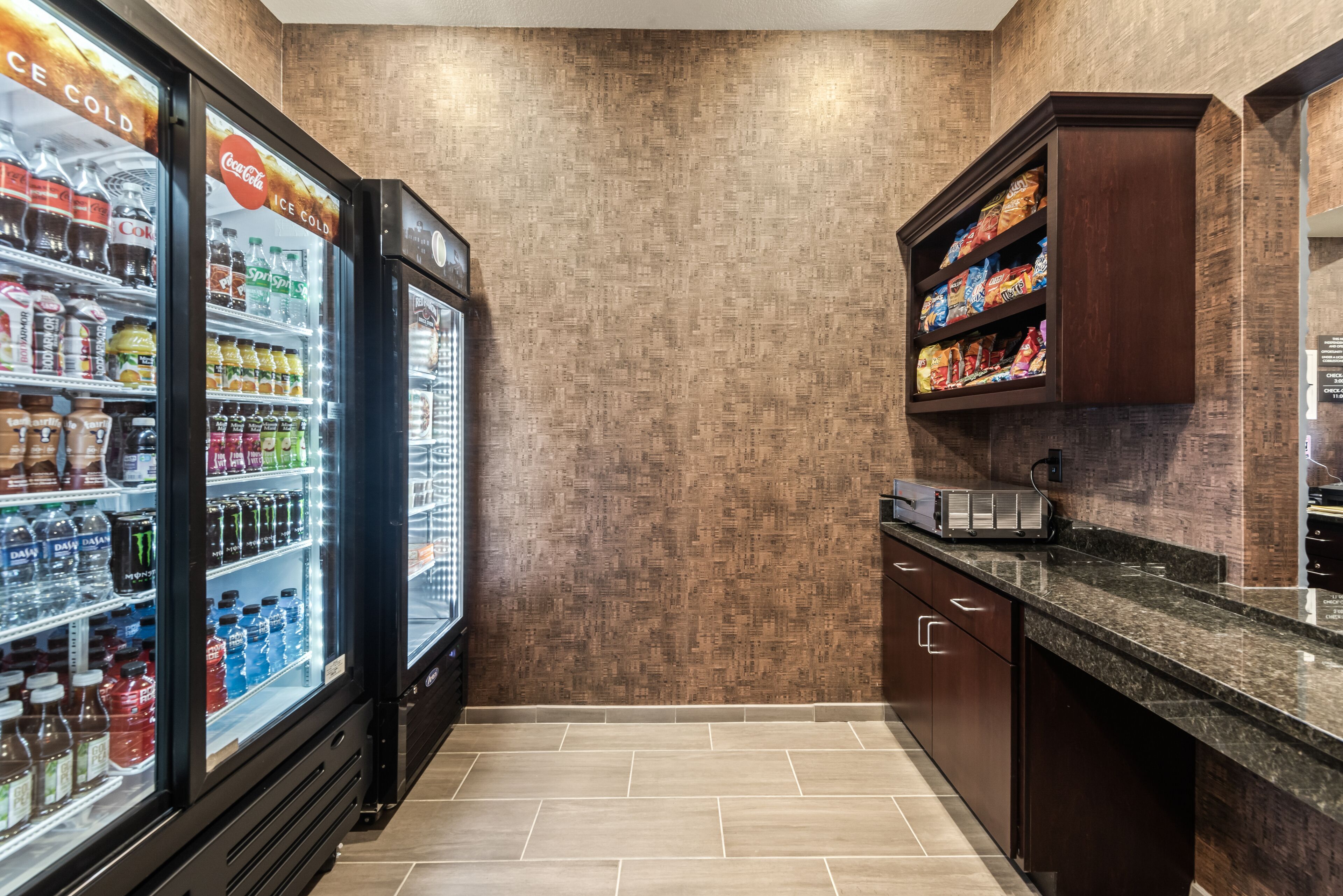 A kitchen area with a refrigerator stocked with beverages, a microwave, and a shelf with snacks.
