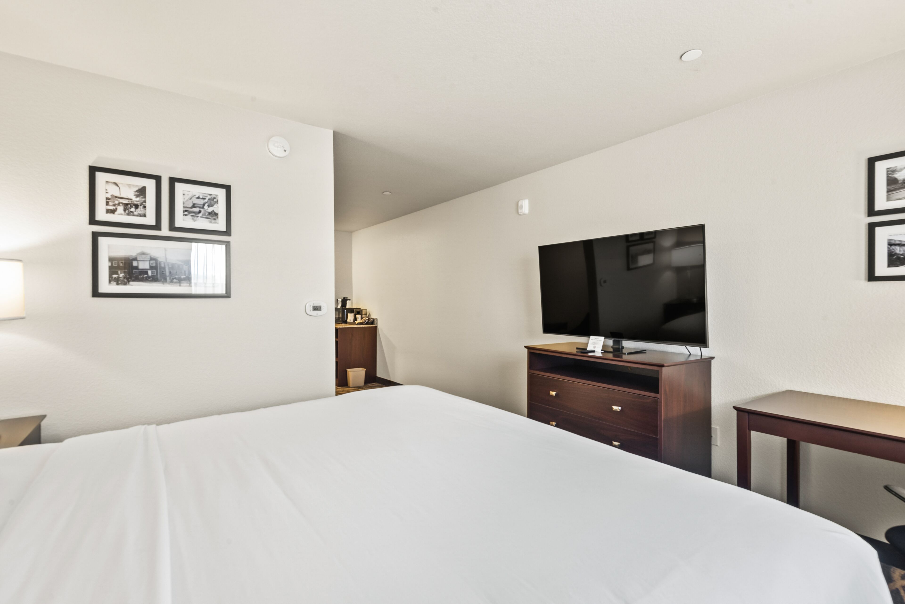 A hotel room with a large bed, a wooden dresser, a flat-screen TV, and framed pictures on the wall.