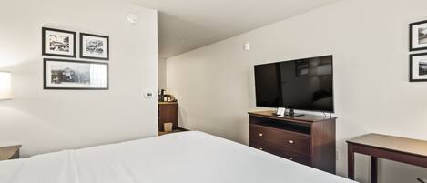 A hotel room with a large bed, a wooden dresser, a flat-screen TV, and framed pictures on the wall.