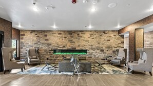 A modern living room with a stone wall, a fireplace, and comfortable seating. - Cobblestone Hotel & Suites - Cullman (Cullman)