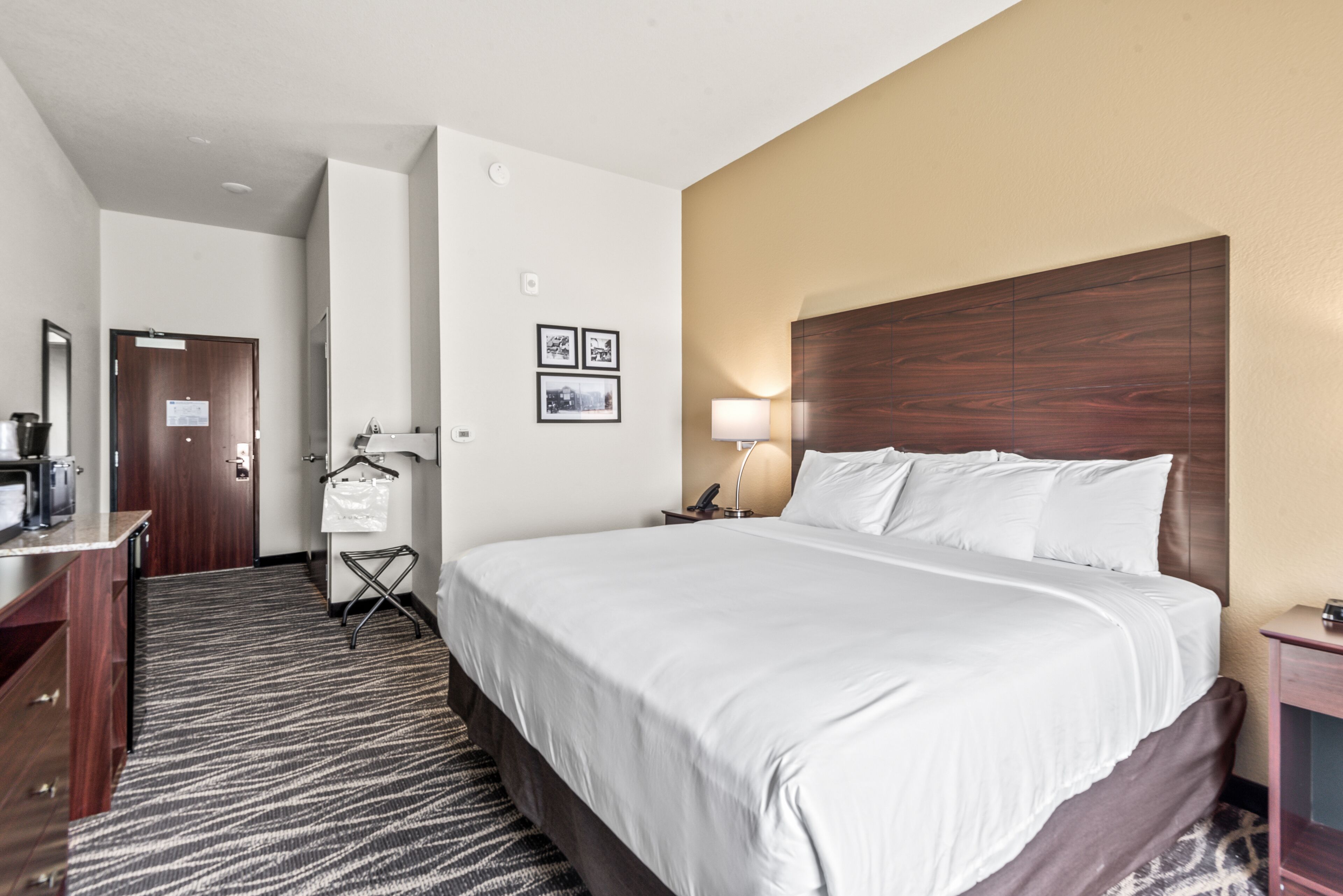 Una habitación de hotel con una cama grande, un escritorio con una silla, un perchero y una puerta.
