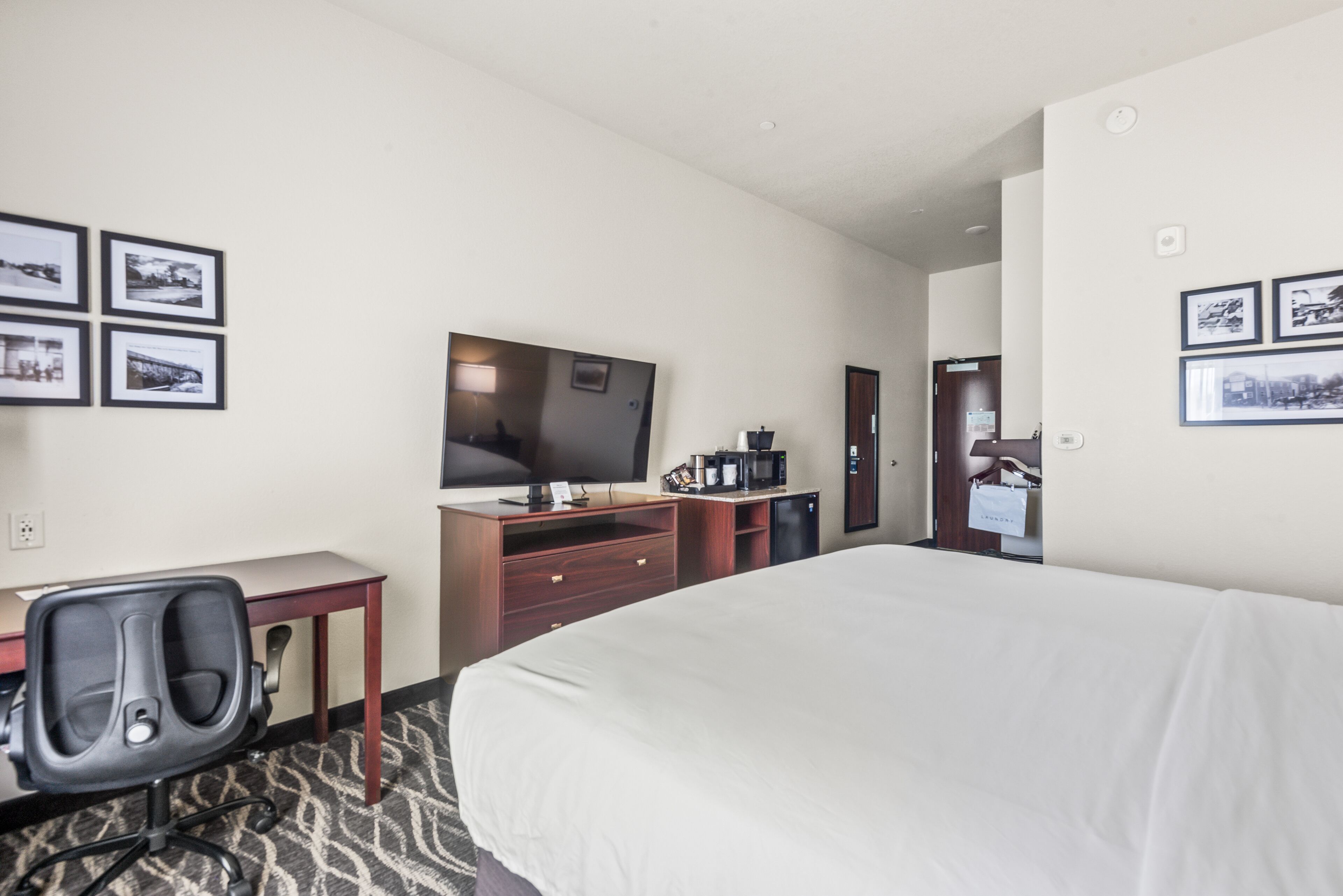 Une chambre d’hôtel avec un grand lit, un bureau avec une chaise, une télévision, une machine à café et des tableaux encadrés aux murs.