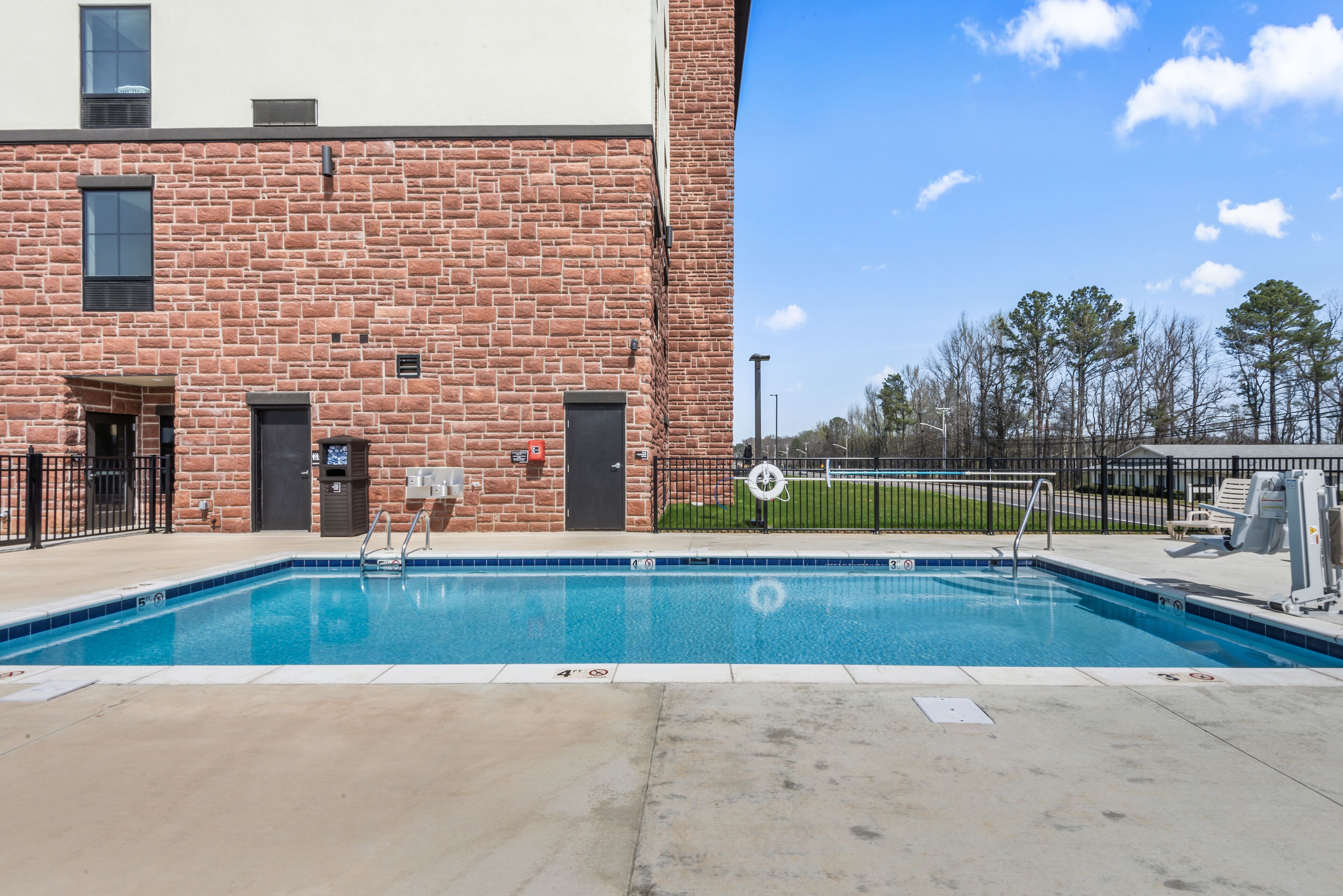 A swimming pool adjacent to a brick building with a clear sky and trees in the background.