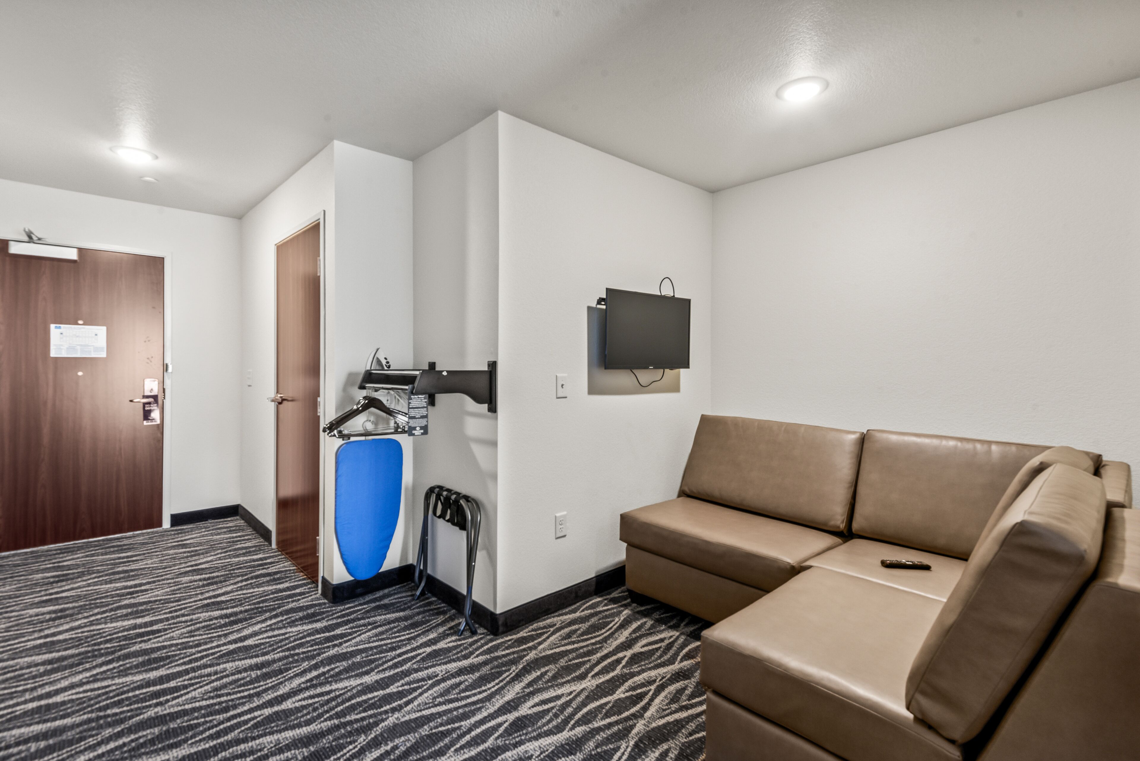 A hotel room with a brown leather sofa, a television mounted on the wall, and a blue exercise machine.